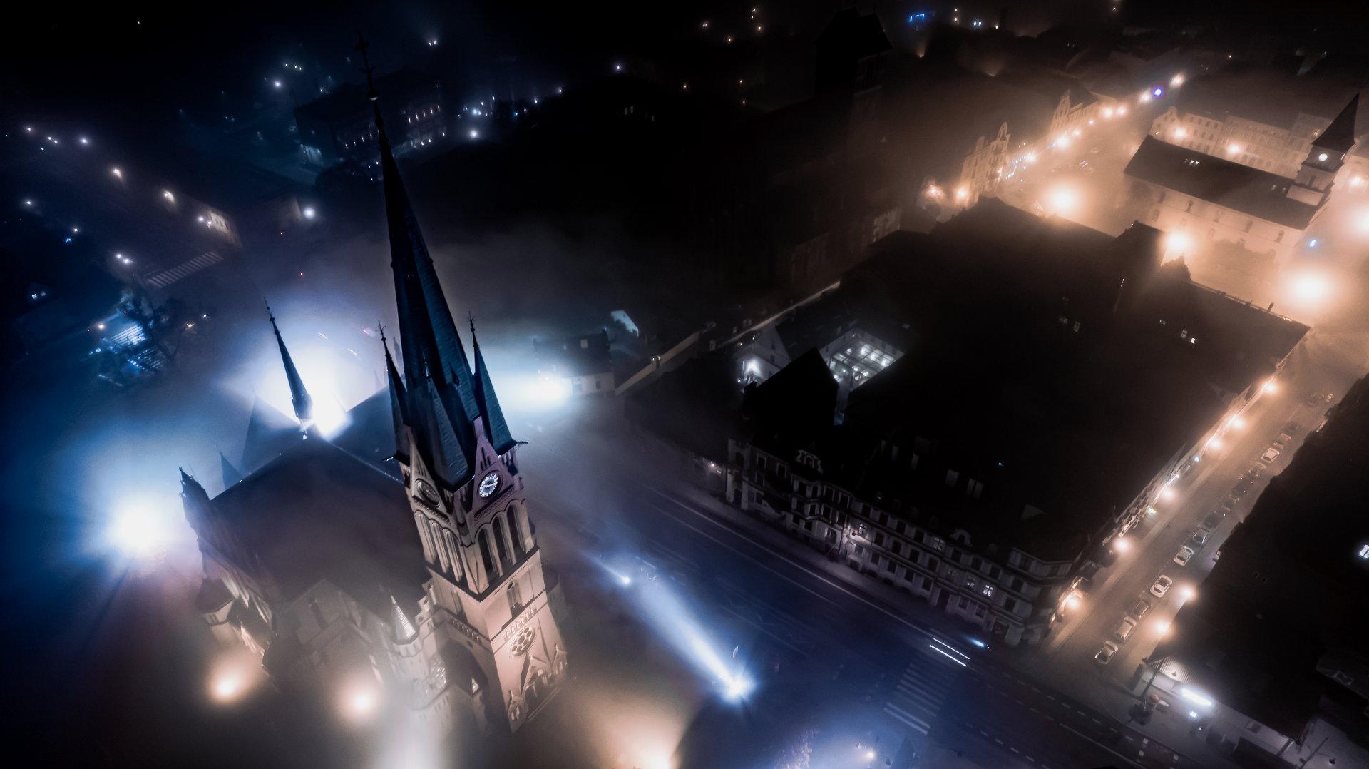Oświetlona wieża kościoła i ulice miasta nocą we mgle